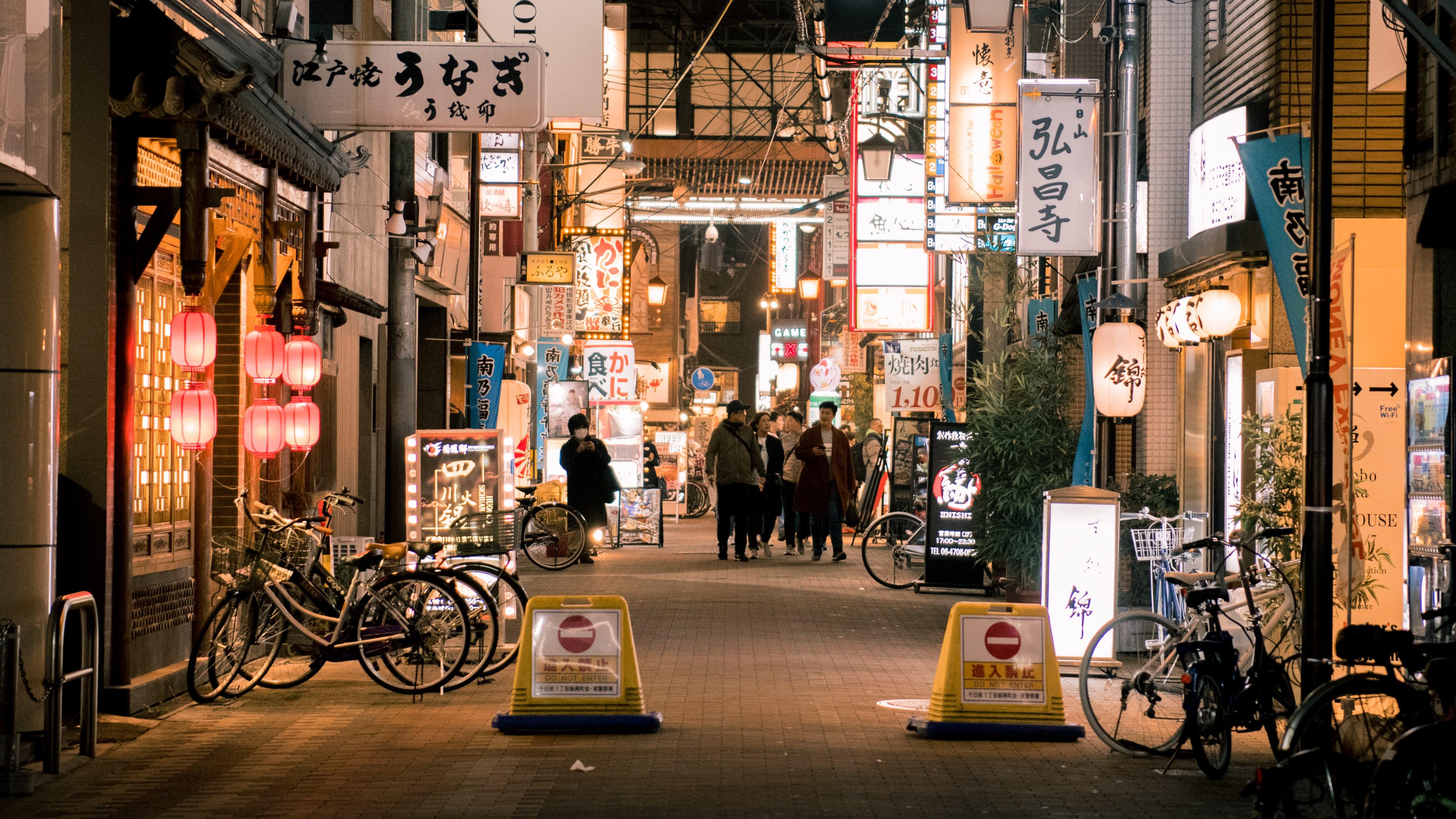 Reference input: an asian city street at night with people and bicycles